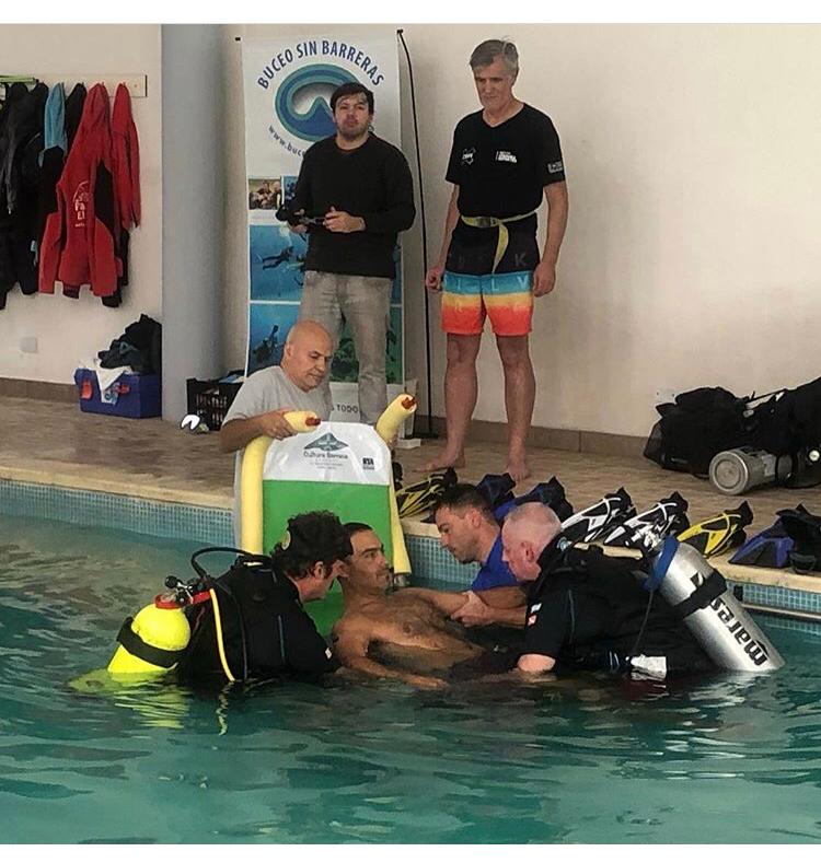 El equipo de Buceo sin barreras sumergiendo en una piscina a una persona con discapacidad motriz. 